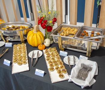 Table decorated for autumn with pumpkins and flowers. Hot Honey Chicken Meatballs, two types of phyllo cup tarts, lemongrass chicken potstickers, and stuffed mushrooms are on display ready to be served.